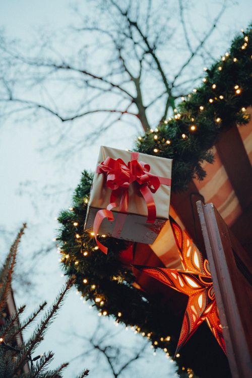 Free A beautifully wrapped gift box with red ribbon and star lantern hang in a festive outdoor setting. Stock Photo