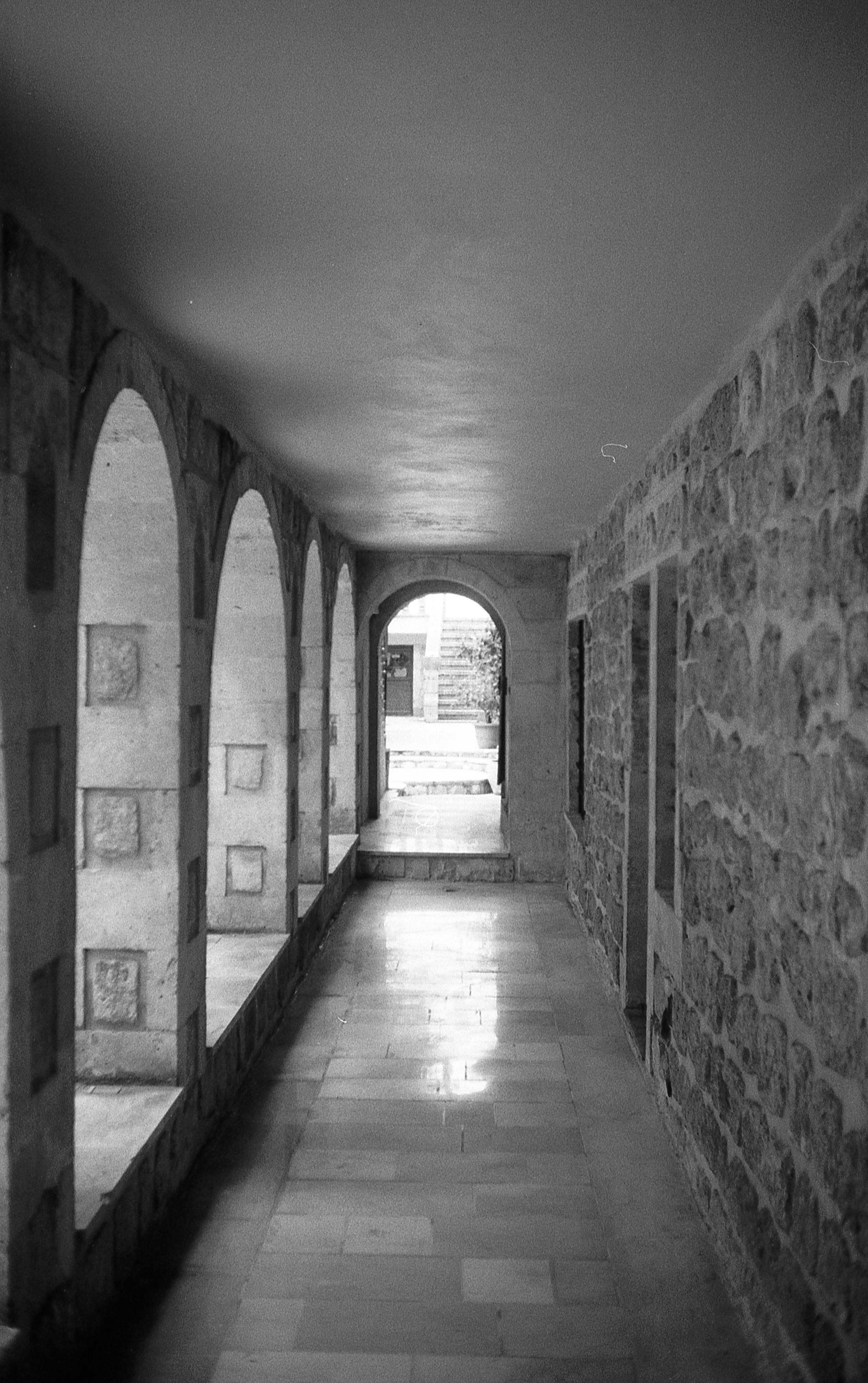 Elegant black and white photo of a stone archway corridor with natural light and shadows.