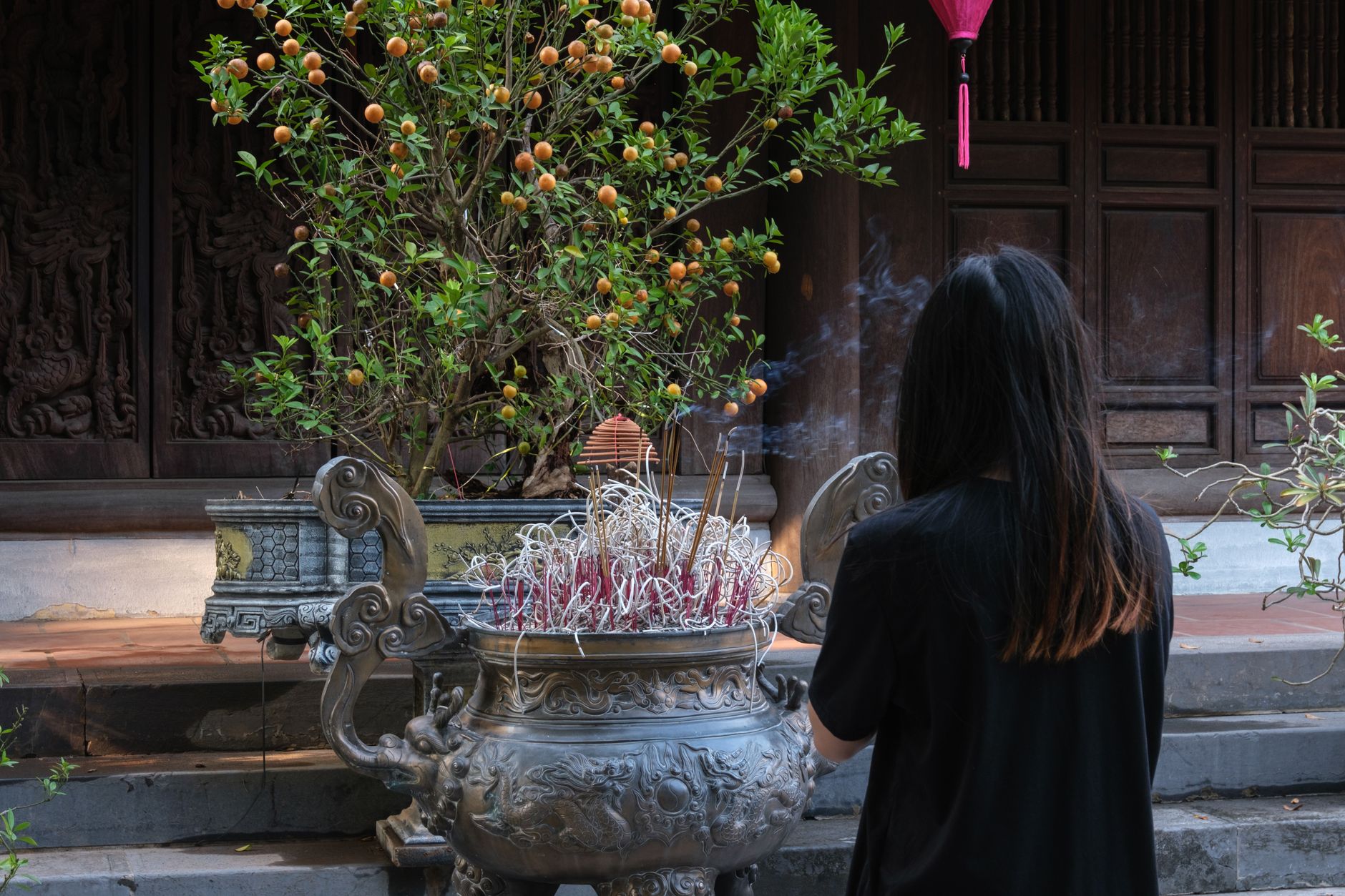 Woman offering prayers at an incense pot in a temple in Hanoi, showcasing cultural traditions.