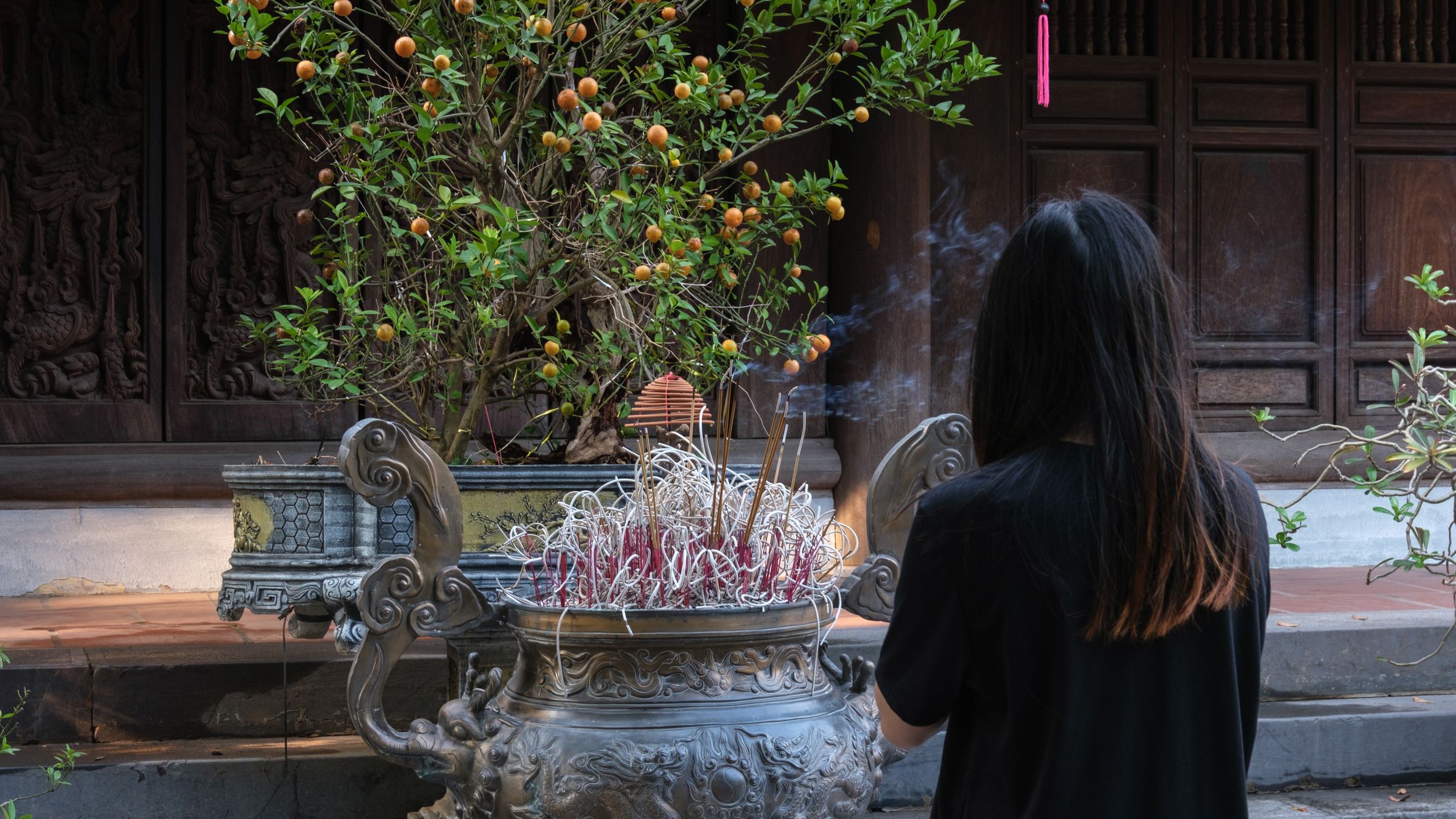 Woman offering prayers at an incense pot in a temple in Hanoi, showcasing cultural traditions.
