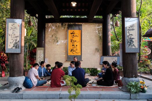 Group of people sitting outdoors at a cultural gathering in Hanoi, Vietnam, surrounded by traditional art.