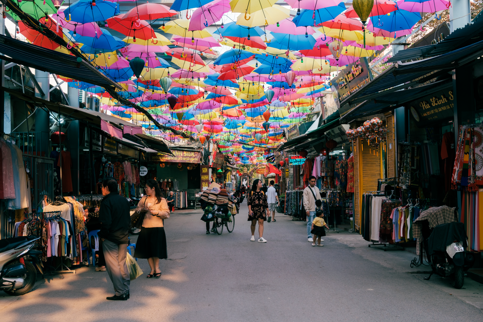 Vibrant outdoor market with colorful umbrellas hanging in Hanoi, Vietnam, showcasing local culture and diversity.