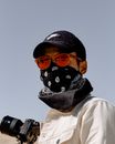 一位戴着太阳镜、帽子和头巾面具的摄影师在户外手持相机