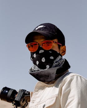 一位戴着太阳镜、帽子和头巾面具的摄影师在户外手持相机