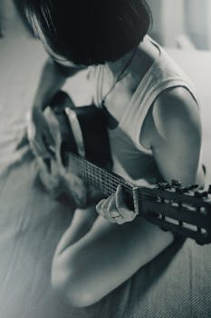 A woman with short hair plays the guitar, creating a moody and artistic black and white portrait.