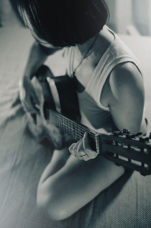 Free A woman with short hair plays the guitar, creating a moody and artistic black and white portrait. Stock Photo