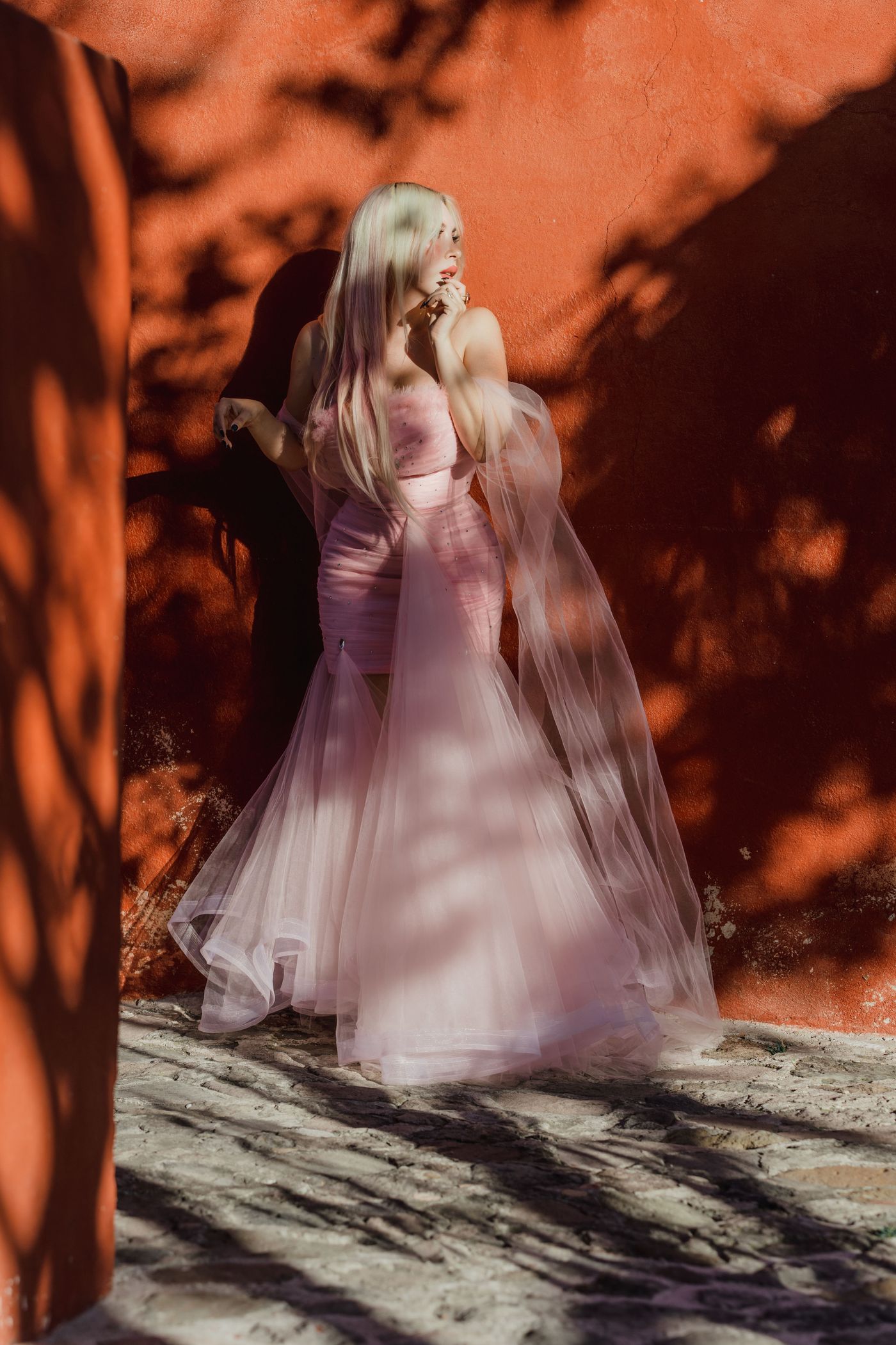 An elegant woman in a pink dress against a red wall — bold blush wedding guest dressing