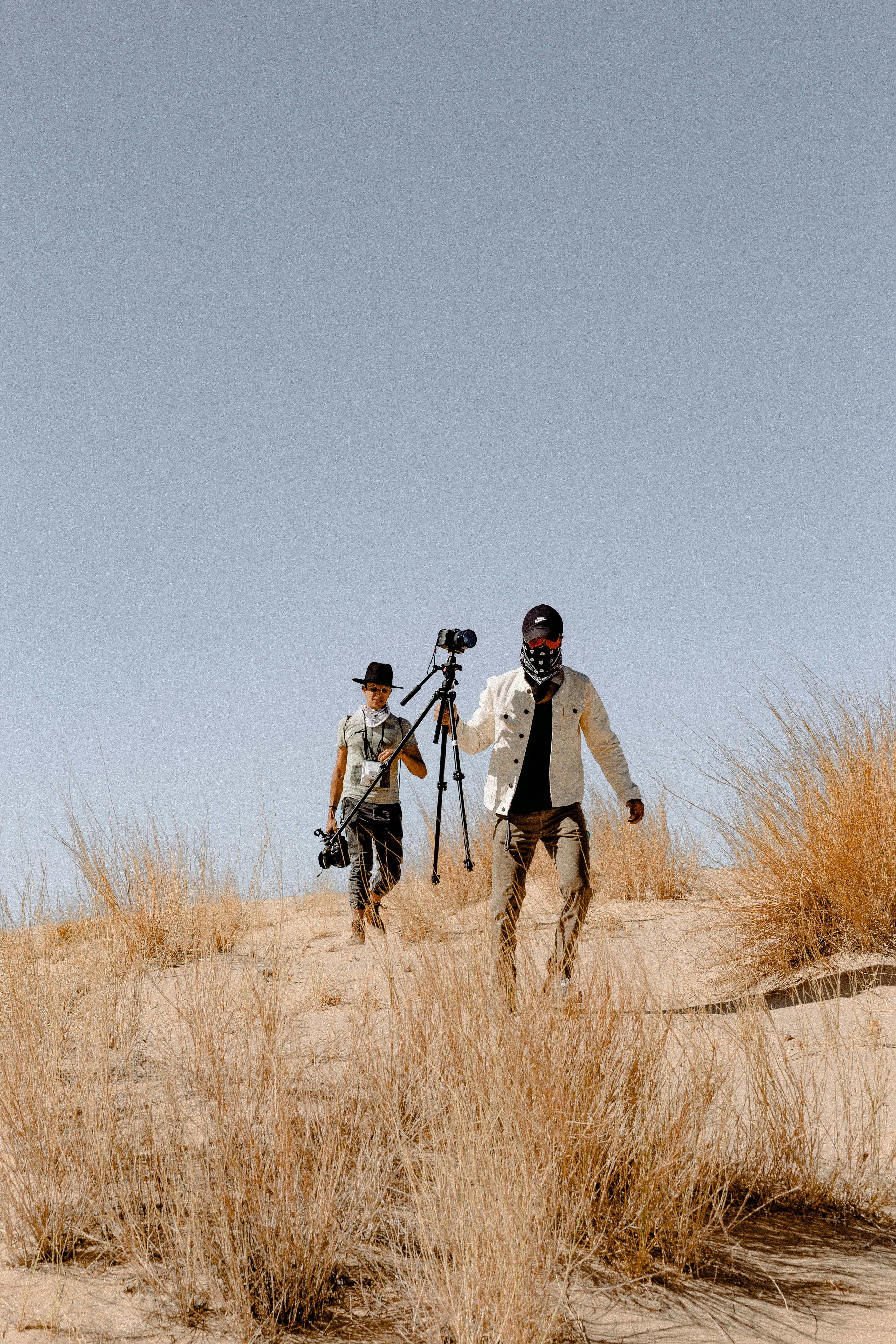 阳光明媚的日子里，两名摄影师带着相机装备徒步穿越沙质沙漠