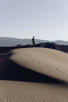 一位独行旅人在日出时分，探索着沙漠沙丘的广阔沙质景观