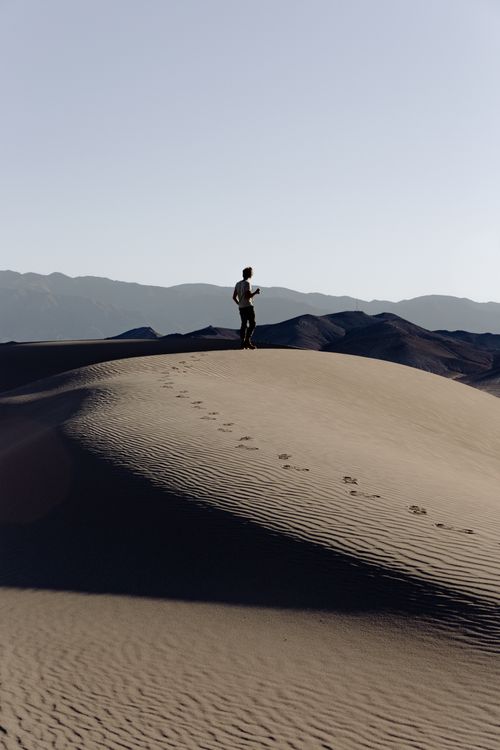 Free A lone traveler explores the vast sandy landscape of a desert dune at sunrise. Stock Photo