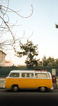 A classic yellow van parked on a quiet street, surrounded by trees and urban elements.