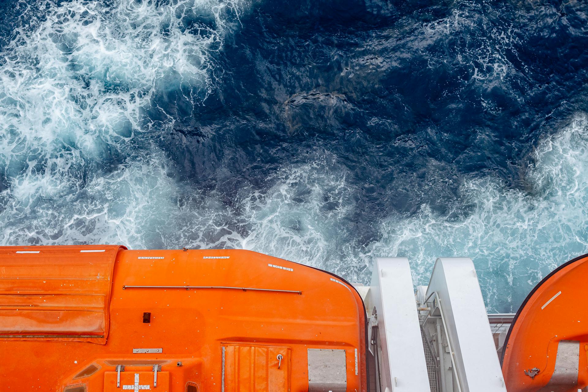 Vibrant photograph of ocean waves viewed from a cruise ship with bright orange lifeboats.