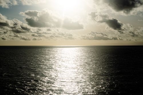Free A serene ocean view at sunset with dramatic clouds and sunlight reflecting on the water. Stock Photo