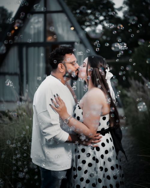 Free A couple sharing a romantic kiss surrounded by floating bubbles outdoors. Stock Photo
