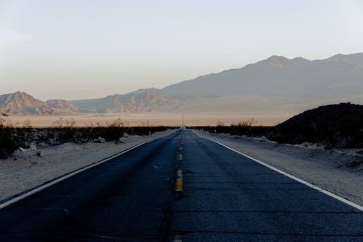 在柔和的日落灯光下，长长的空旷的沙漠公路向山脉延伸