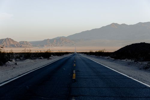 Free Long empty desert highway stretching towards mountain range under soft sunset light. Stock Photo