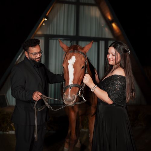 Free Elegant couple posing with a horse during a nighttime photoshoot. A-frame structure in background. Stock Photo