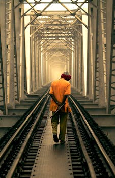 一个男人穿着休闲装，独自走在被钢结构框起来的铁路桥上