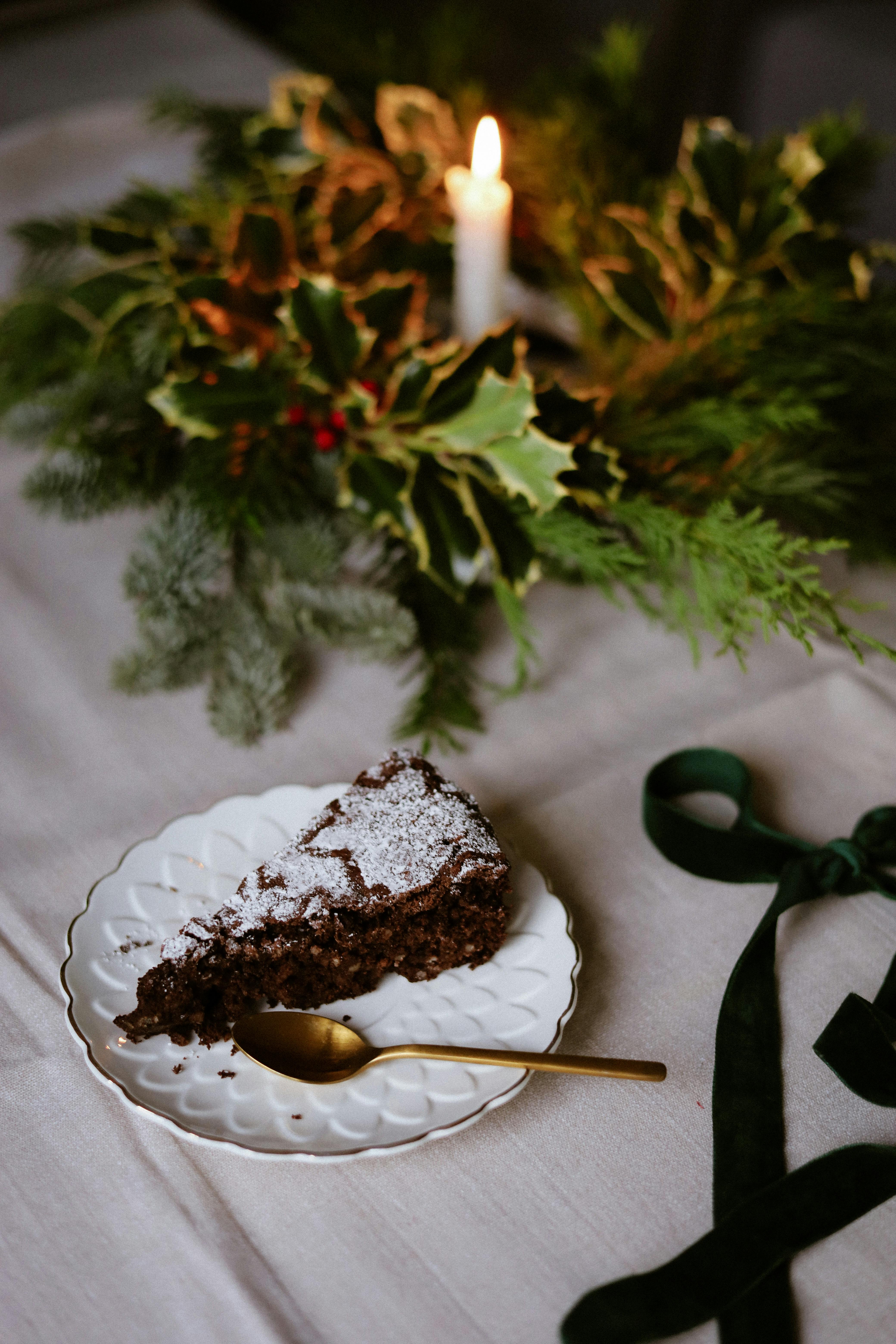 A piece of chocolate cake on a festive holiday table with greenery and candlelight.