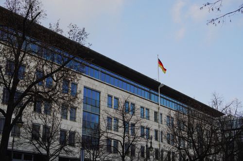 Free A modern building with a German flag, surrounded by bare trees under a clear sky. Stock Photo