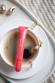 Pink lip tint on coffee cup with gold jewelry on a cozy surface.