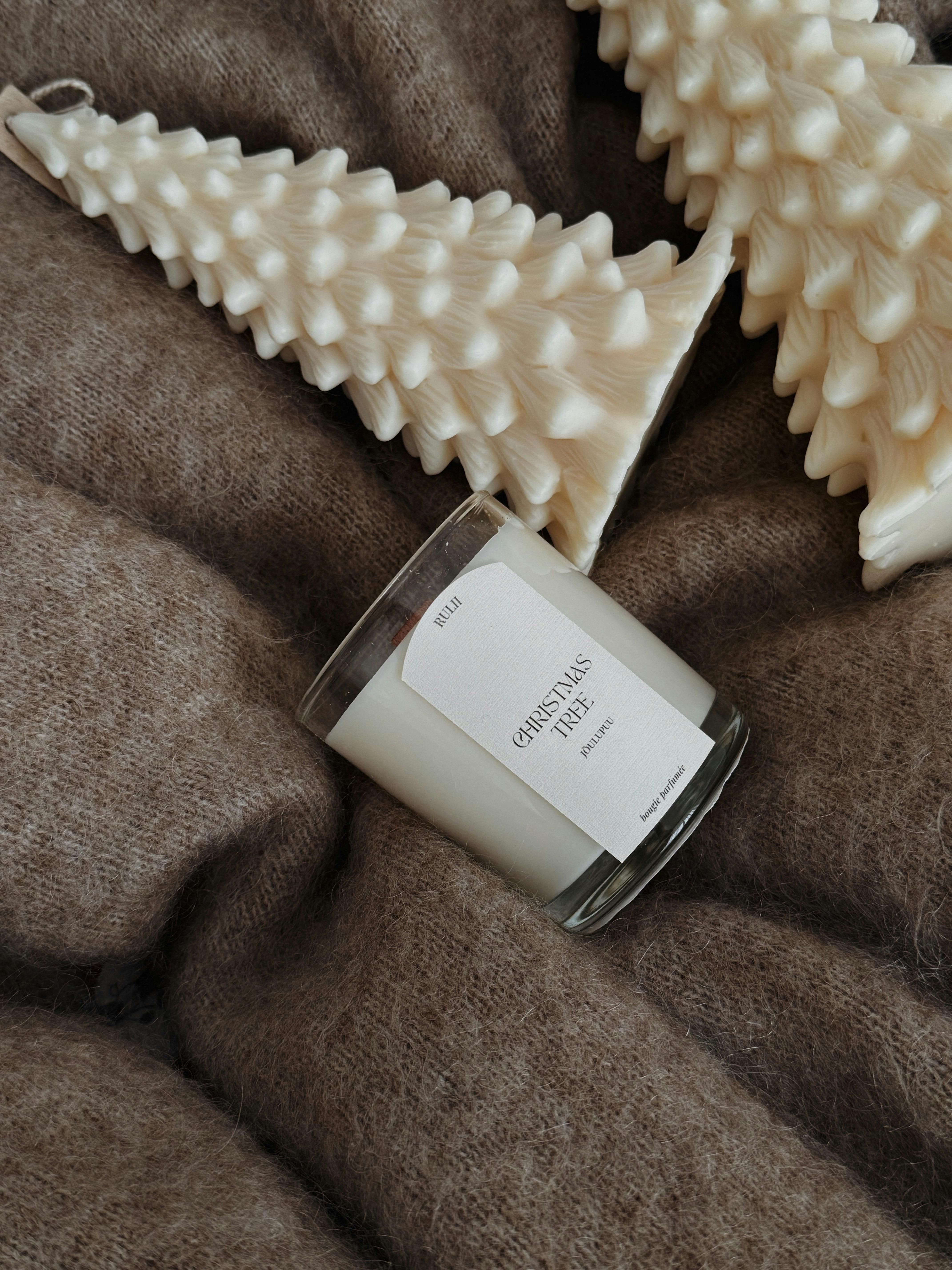 Elegant white candle and tree decorations on a soft brown fabric, perfect for the festive season.