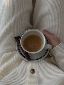 A warm cup of coffee cradled in hand, paired with a chocolate wrapper.