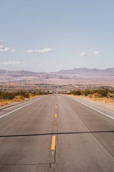 一条长长的直路穿过沙漠，在晴朗的天空下延伸向遥远的山脉