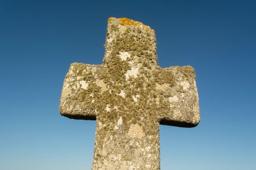 Free A rustic stone cross covered in moss stands against a clear blue sky, symbolizing tranquility. Stock Photo