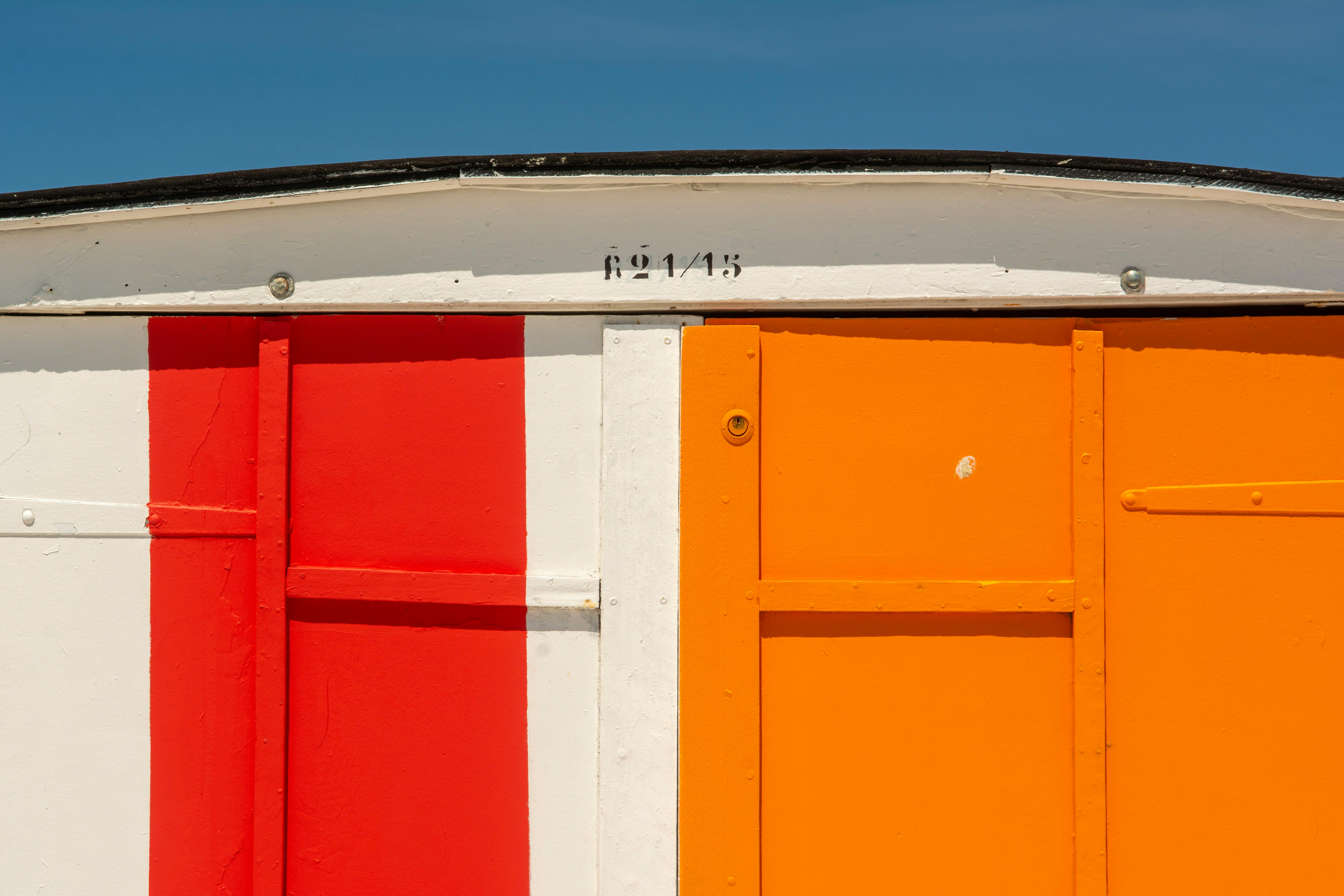 Vibrant red and orange doors of a beach cabin under blue sky in Le Havre, France.