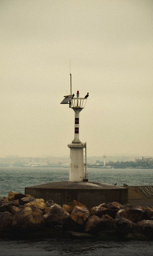 Free Solitary lighthouse towering over rocky shore amidst a tranquil sea view. Stock Photo