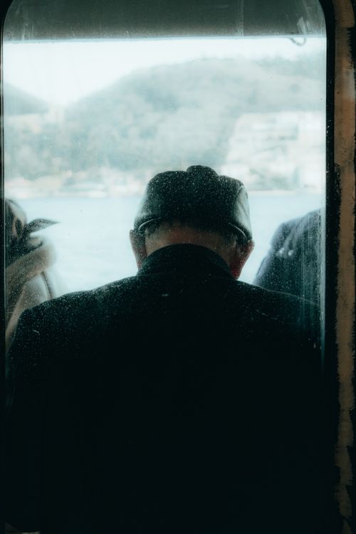 Free A silhouette of a man wearing a cap, viewed from behind, gazing out from a ferry window. Stock Photo