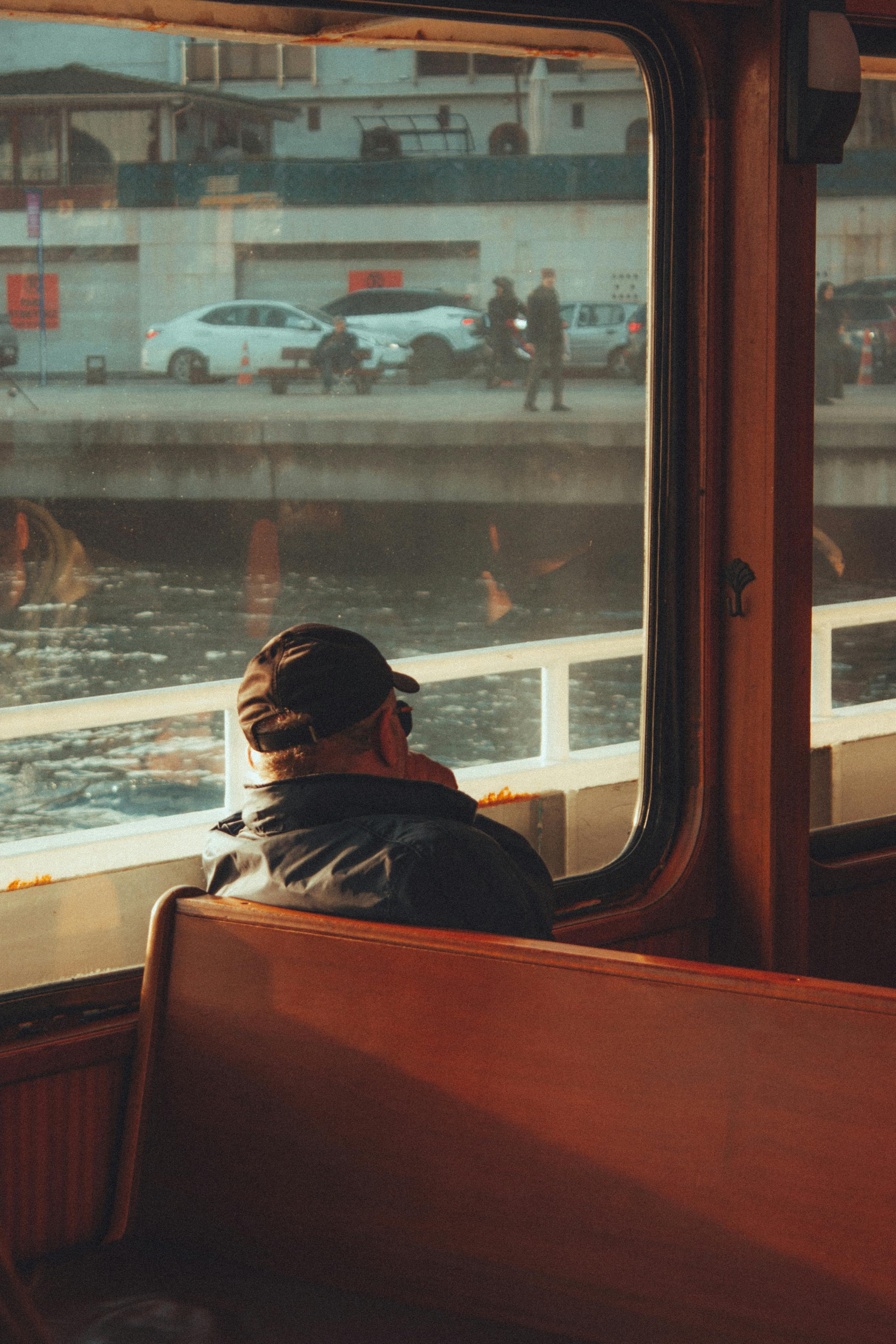 A man enjoys a scenic view from a ferry window on a river journey.
