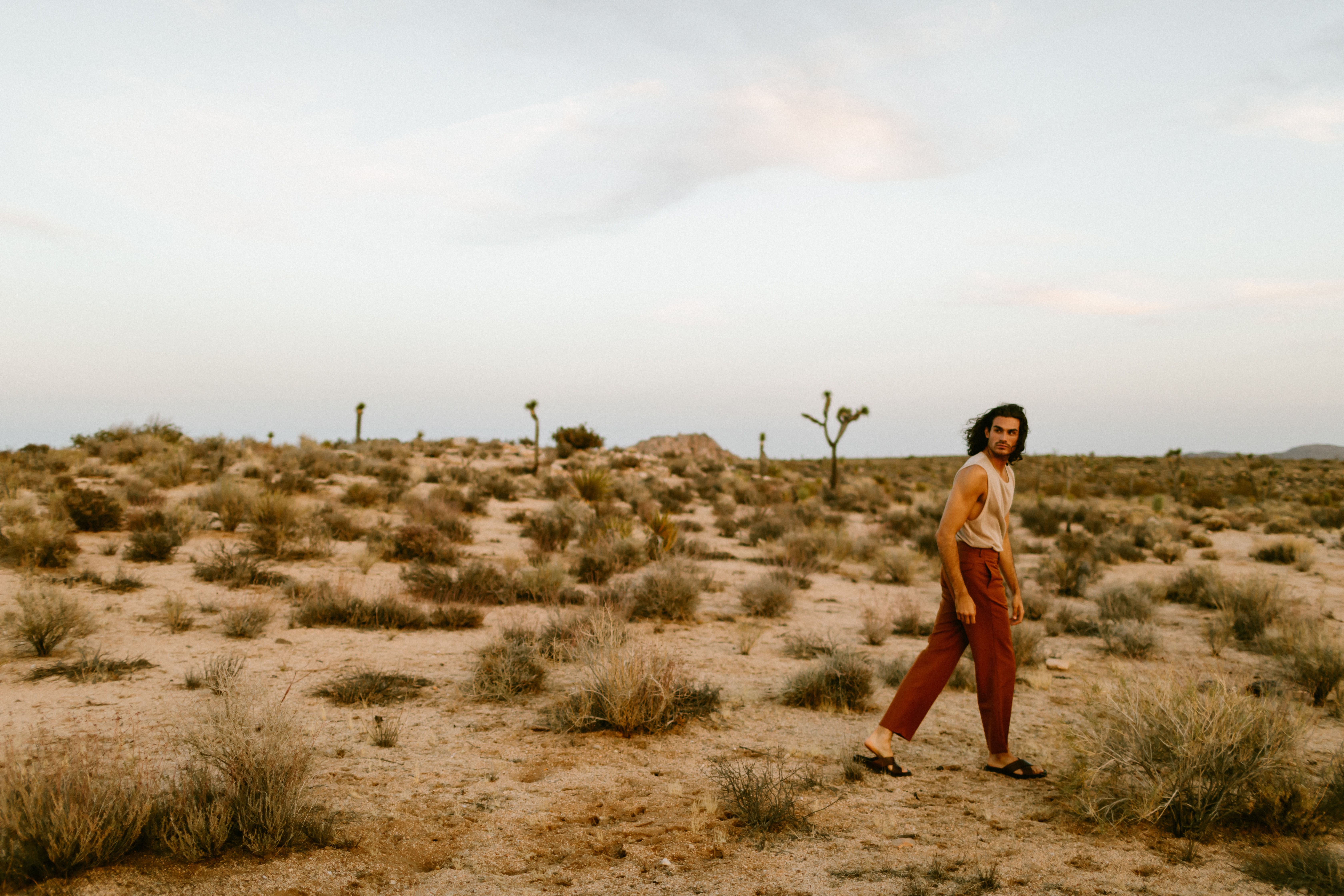 Fashion-forward man strolling through iconic Joshua Tree desert at sunset, showcasing earthy tones.