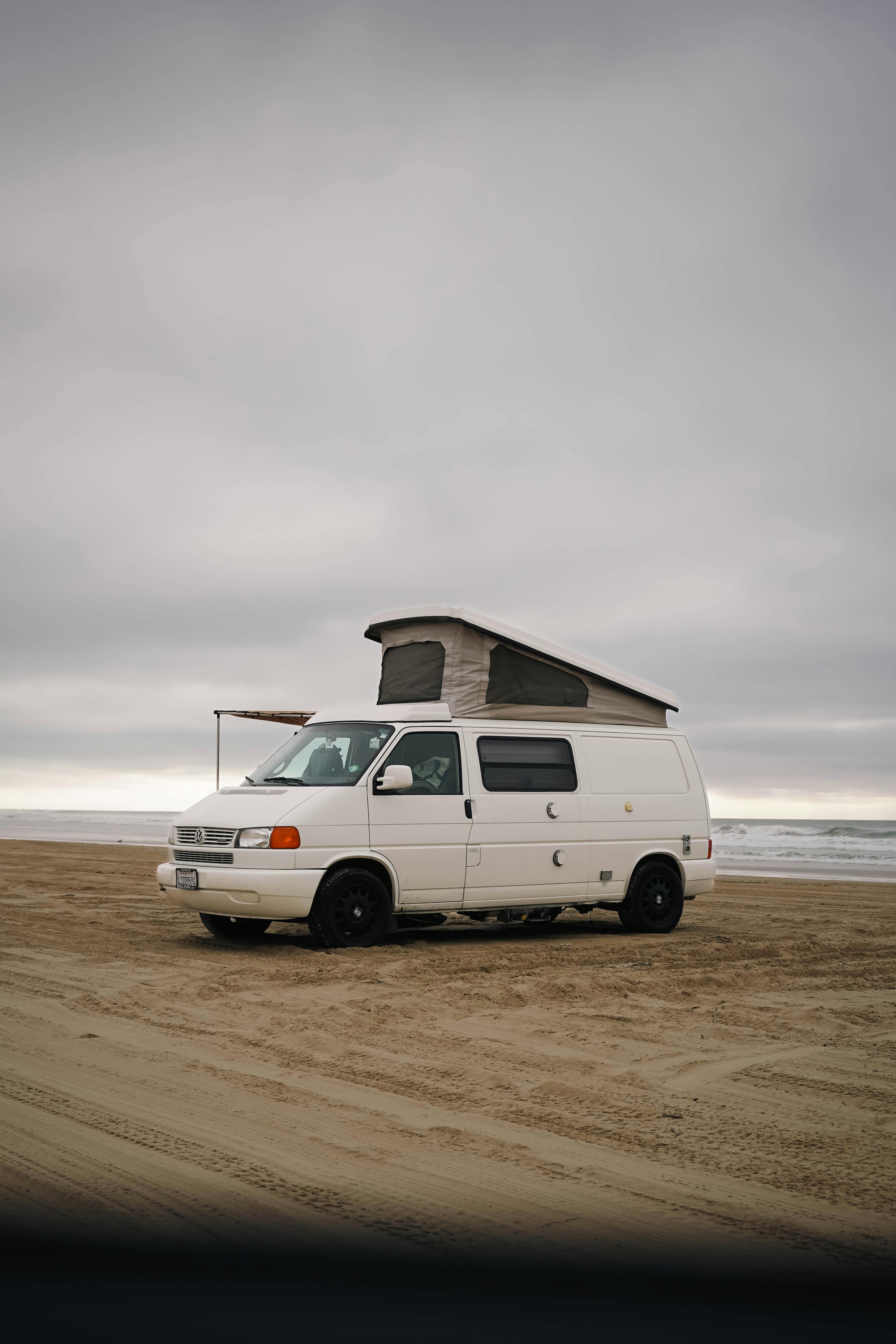 A classic white Volkswagen van parked on Oceano Beach, California, under a cloudy sky.