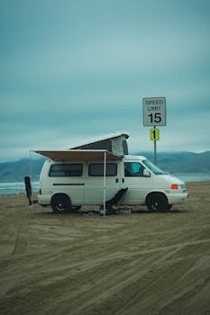 A classic Volkswagen van parked on a sandy beach in Oceano, California, under a teal sky.