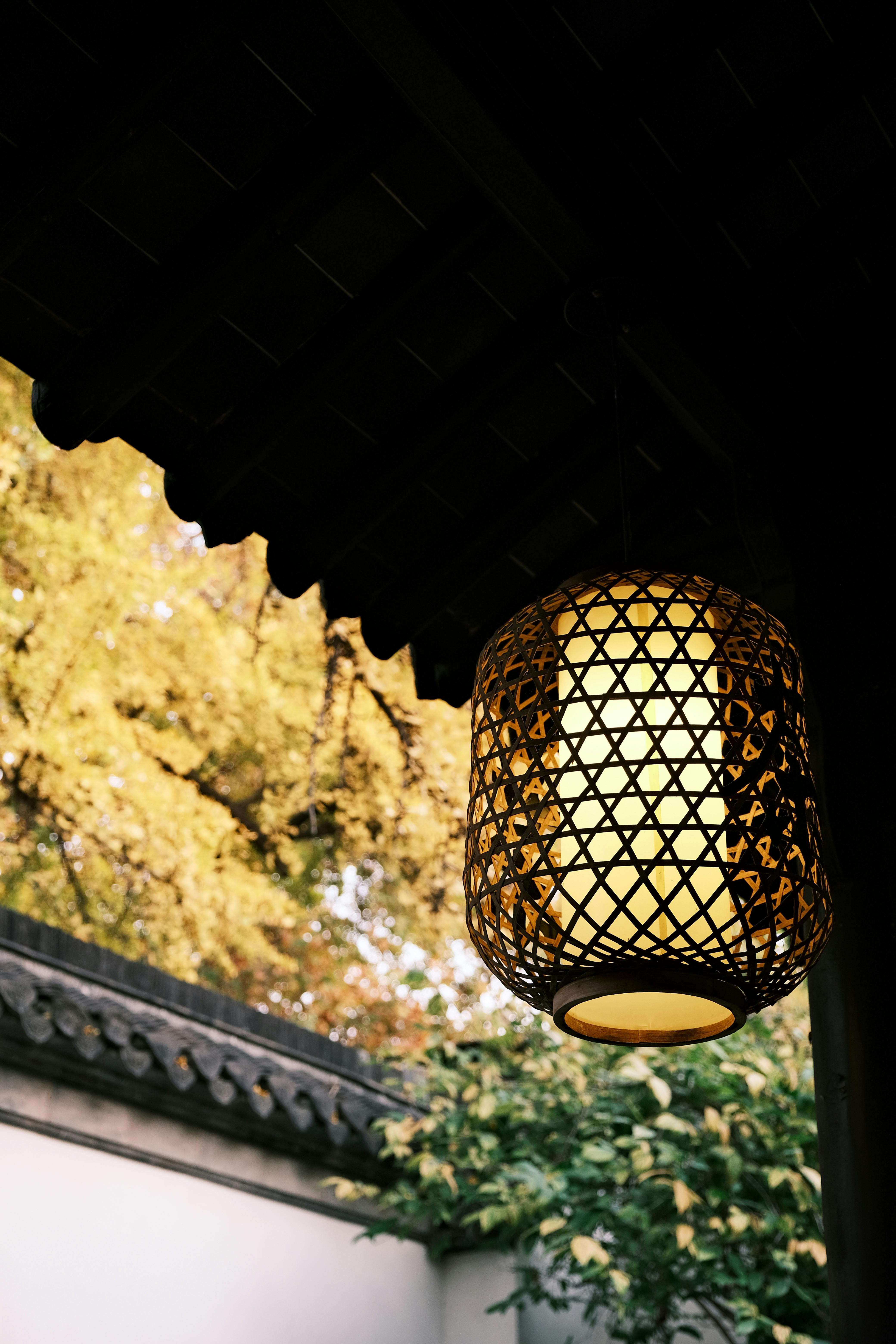 Elegant woven lantern hanging outdoors with golden autumn leaves.