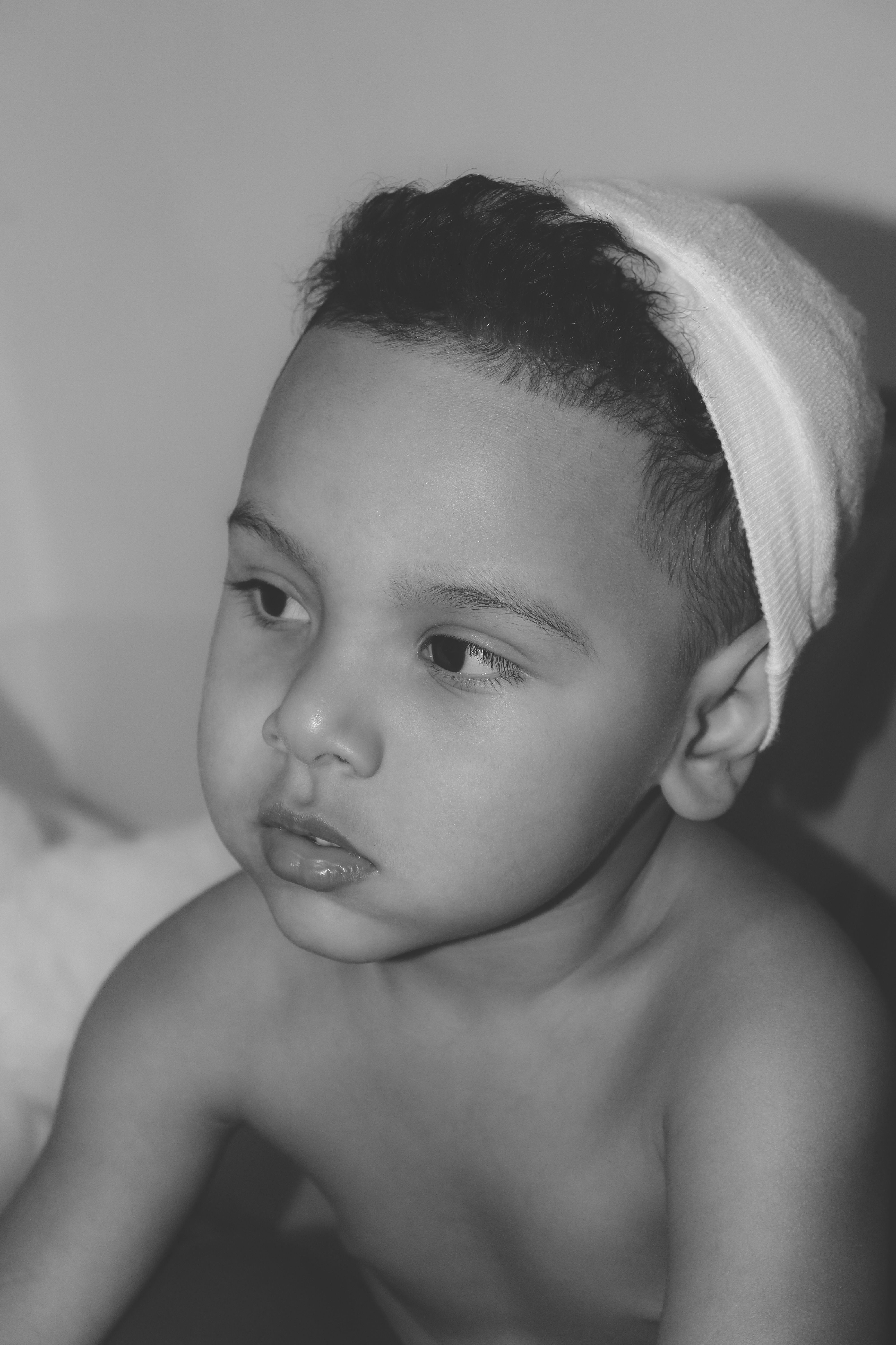 Black and white portrait of a young child with a towel on head, serene expression.