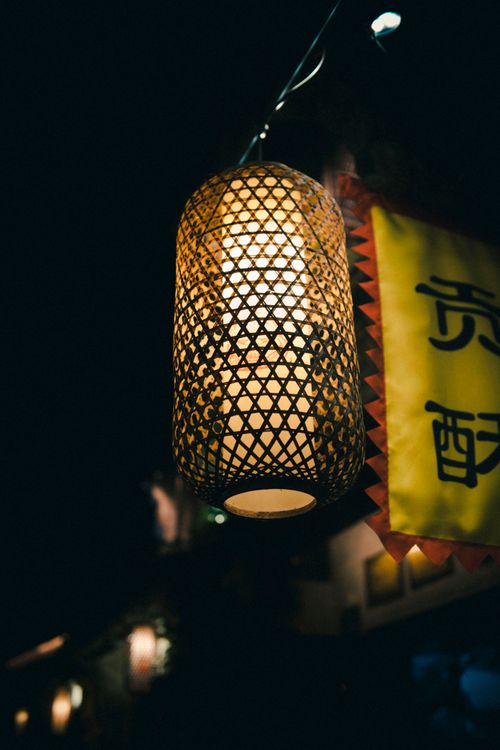 Free A beautifully crafted lantern hangs glowing at night, adding warmth and ambiance to a street scene. Stock Photo
