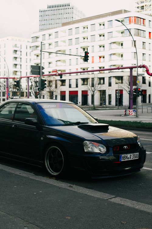Free Stylish black sedan parked in a modern urban area with tall buildings in the background. Stock Photo