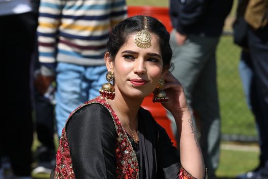 Woman in traditional outfit with jewelry, outdoors in a bright setting.