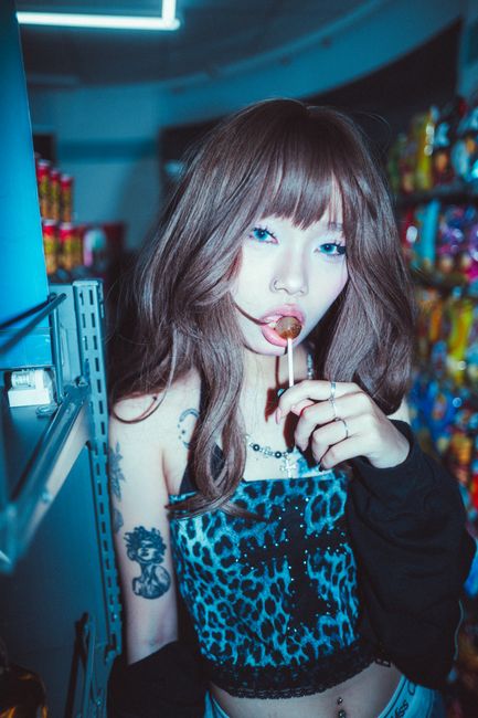 Trendy young woman with tattoos holding lollipop in a grocery store.