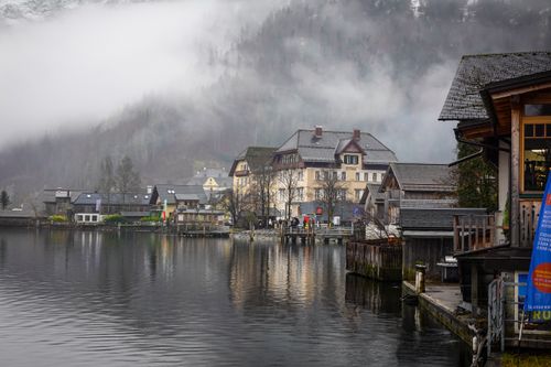 Free A picturesque view of a mountain village by the lake enveloped in winter mist, featuring charming architecture. Stock Photo