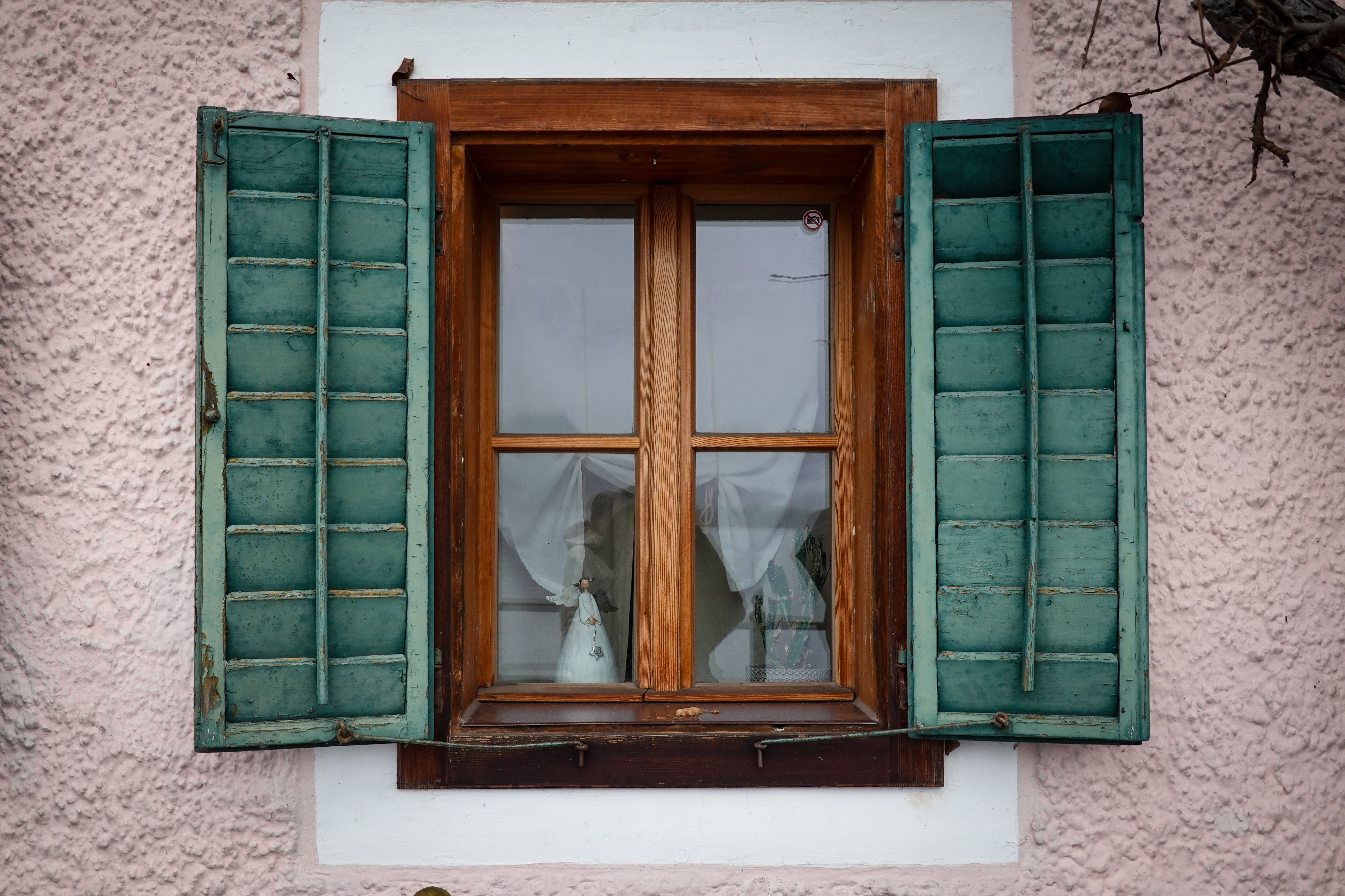 Rustic wooden window with open green shutters on a textured wall.