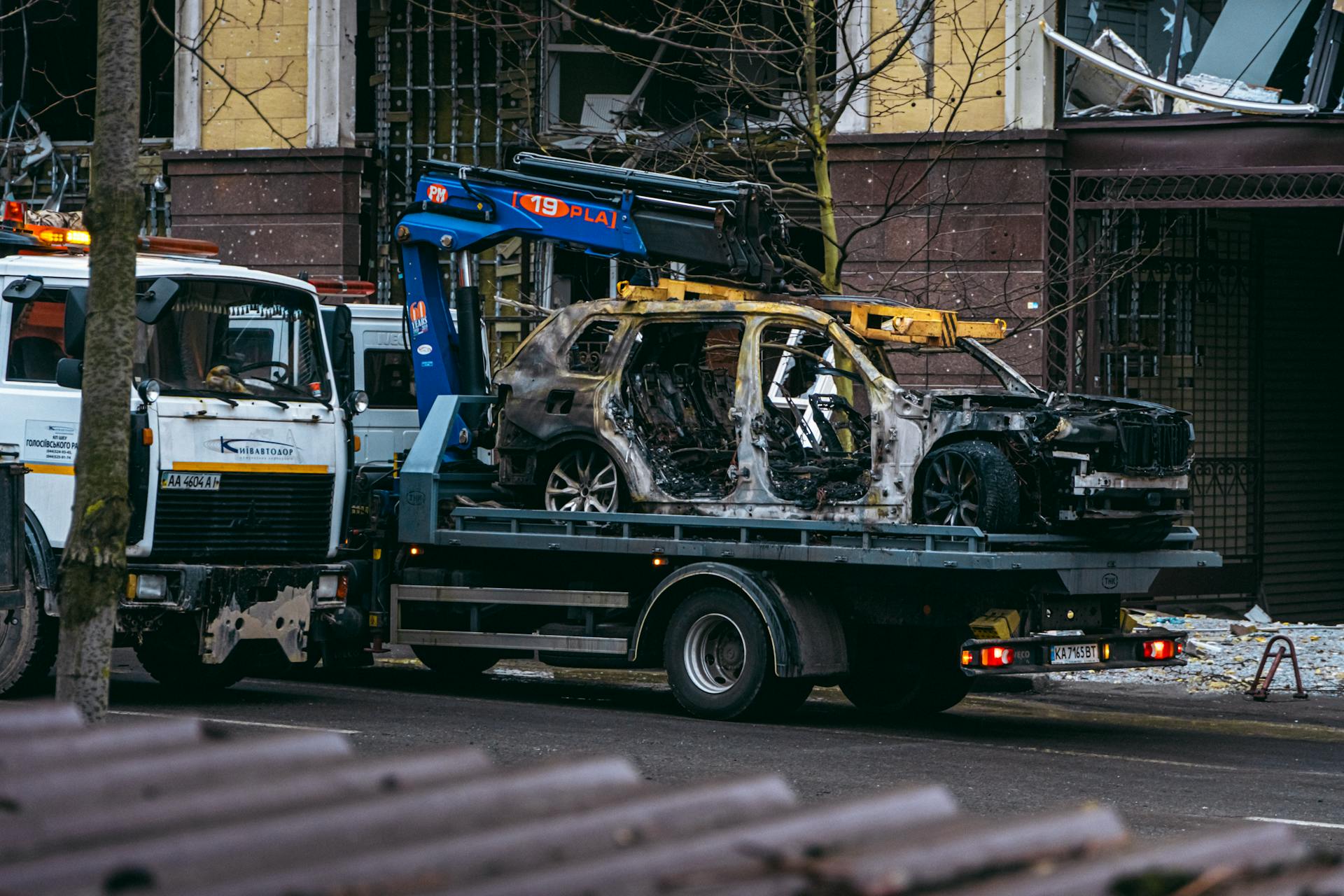 A burnt car is towed on a street in Kyiv, highlighting the aftermath of conflict.