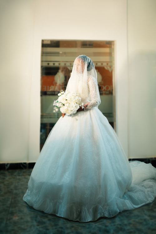 Free Stunning bride in a white dress holding a bouquet, captured indoors. Stock Photo