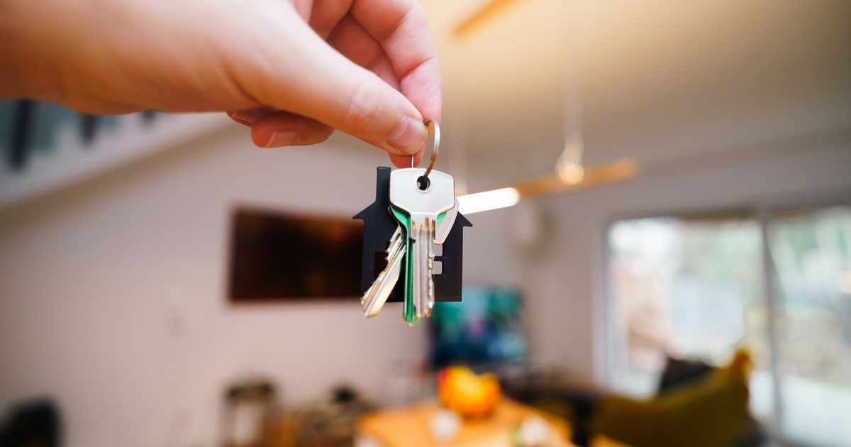Hand holding house keys in front of a blurred living room interior