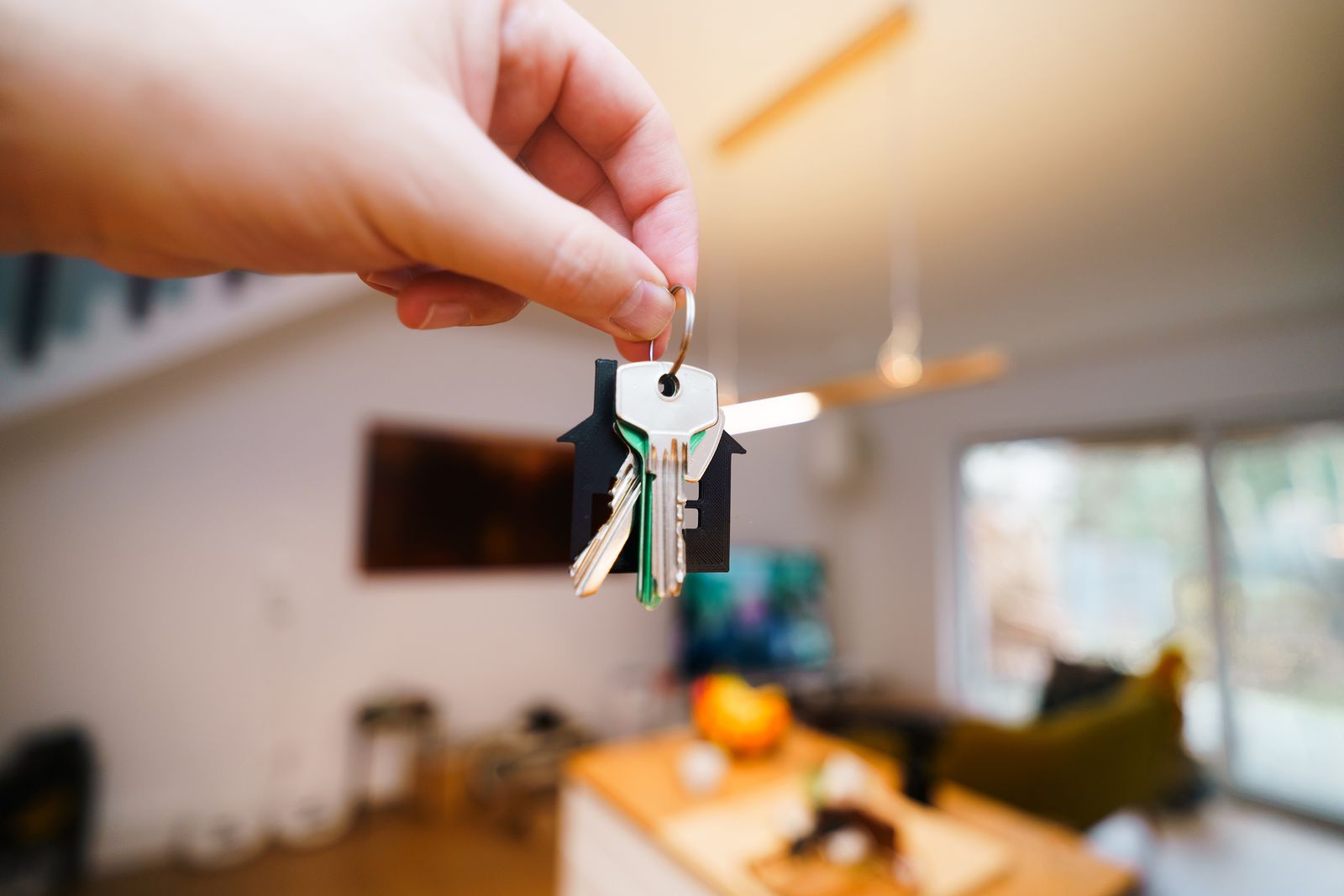 Free A hand holds keys with a house keychain inside a modern, well-lit living space. Stock Photo