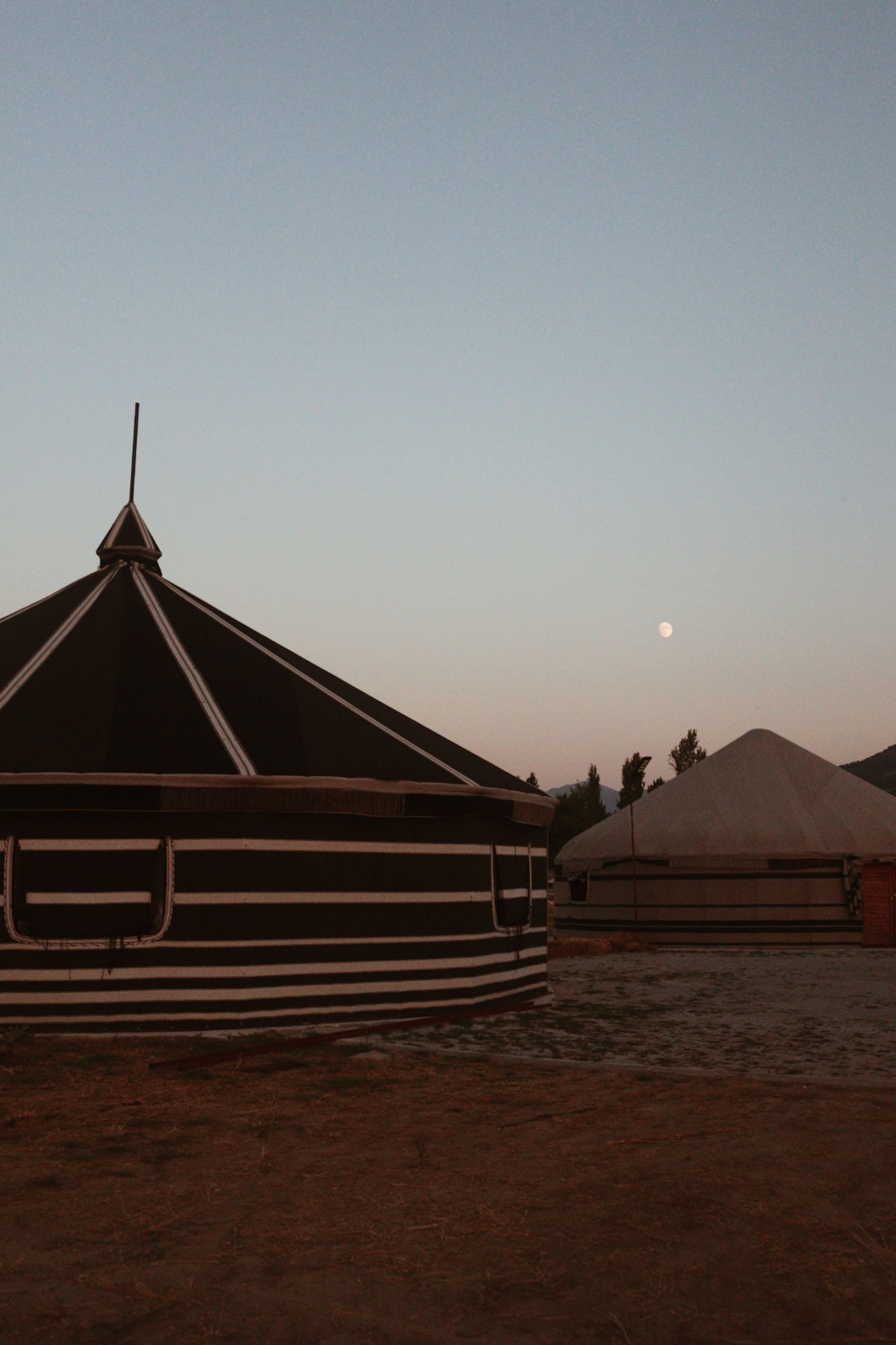 Captivating landscape of traditional yurts under a serene dusk sky with a full moon.