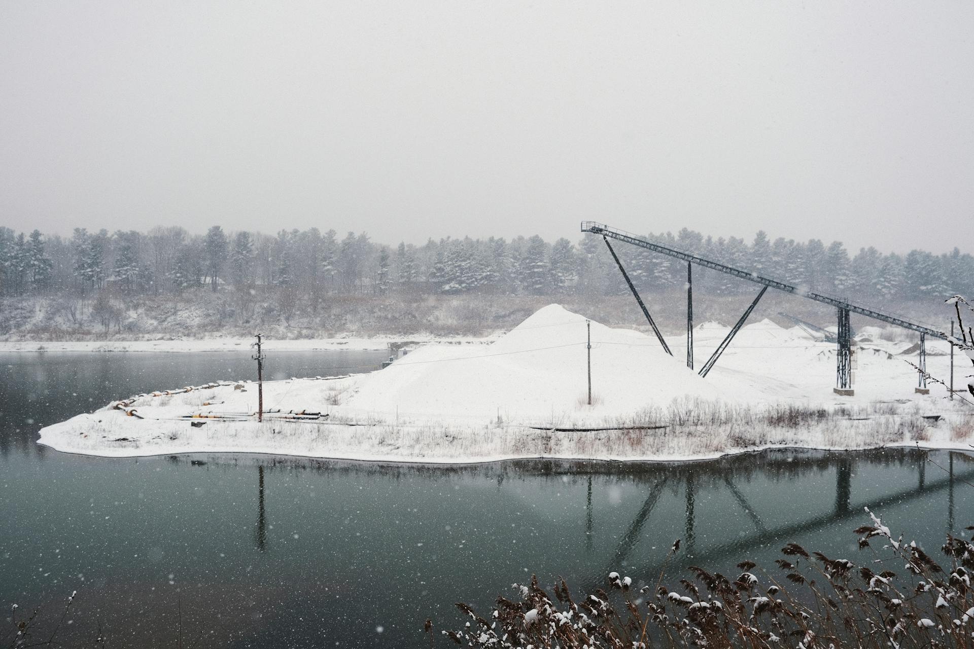 Snow-covered industrial area with lake and conveyor belt during winter snowfall